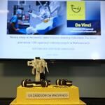 Na pierwszym planie żółto-brązowy tort z etykietą „100 zabiegów Da Vinci w KCO”, w tle prezentacja o operacjach wykonywanych przez robota